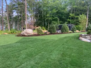 Boulder accent planting along lawn edge with utility trailer