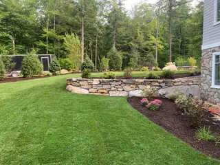 Curved fieldstone wall with pink sedum bed at lakeside home