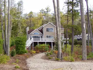 Elevated home in wooded setting with rustic fencing and landscaping