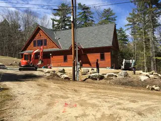 Excavator and crew grading site at cedar-shingled home