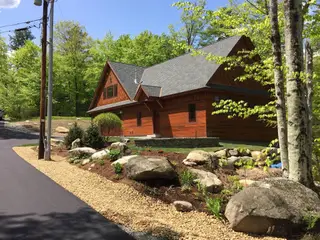 Finished cedar home with boulder-lined gravel driveway