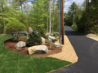 Landscaped driveway entrance with evergreen and boulder plantings