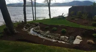 Stone-lined stream bed leading to lakeside lawn