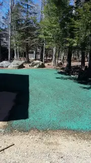Hydroseeded lot with boulders near wooded driveway