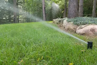 Sprinkler irrigating sloped lawn by stone wall