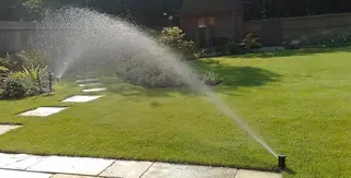 Sprinkler near stone pathway and garden bed