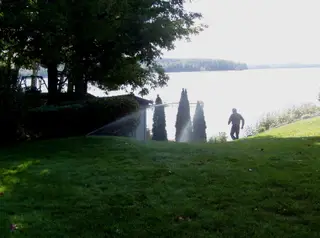 Sprinklers irrigating lawn near lakeside shed at sunrise
