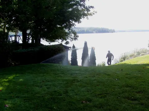 Sprinklers irrigating a lawn near a lakeside shed at sunrise