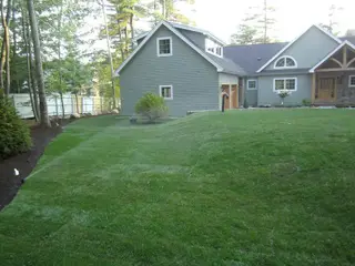 Sprinklers irrigating sloped lawn near gray house