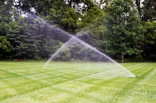 Two sprinklers crossing over striped lawn