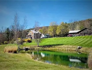 Farmhouse property with striped lawn and pond