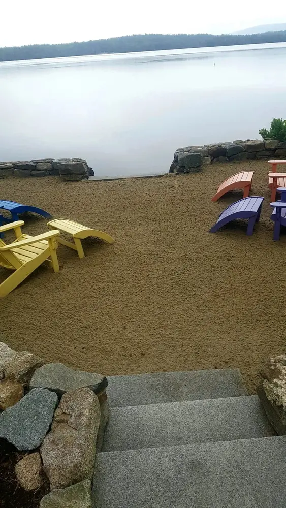 Colorful Adirondack chairs waiting on a sandy lakeside beach