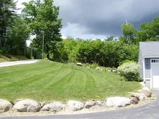 Sloped striped lawn with new plantings and boulders