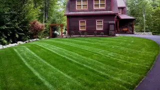 Striped lawn before dark-red farmhouse-style home