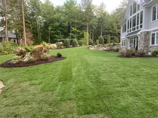 Striped lawn leading to stone wall and lake house
