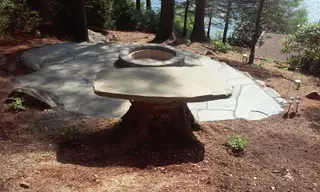 Circular fire pit patio with stump table near lake