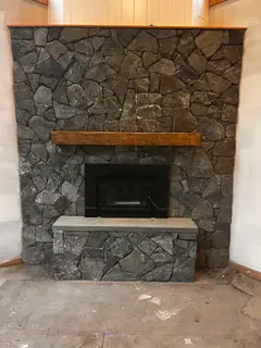Finished dark stone fireplace with wood mantel beam