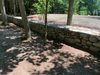 Long dry-stacked stone wall along wooded driveway