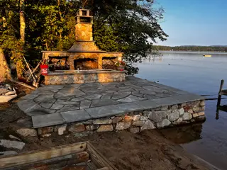 Outdoor stone fireplace and chimney beside lake