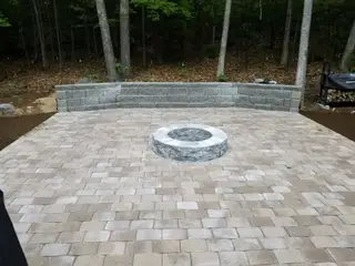 Paver patio with fire ring against curved stone wall