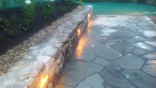 Illuminated stone wall by pool at dusk