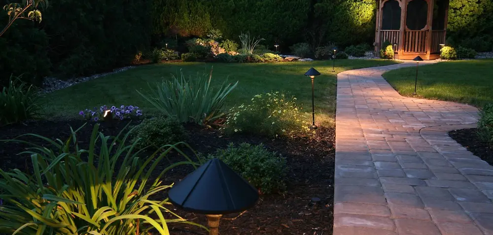 Lit paver walkway leading through landscaped garden beds to a gazebo at dusk