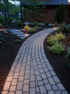 Lit paver walkway through garden beds at dusk