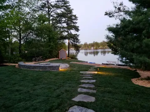 Lit stone patio wall and pathway leading to a lakeside dock