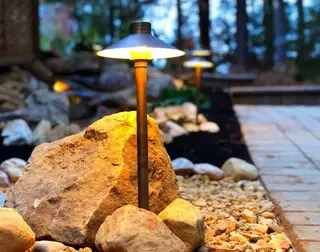 Path light glowing beside boulder and gravel bed