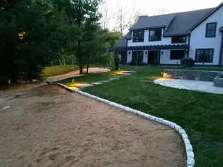 Path lights framing a paver-edged patio behind a shingled home
