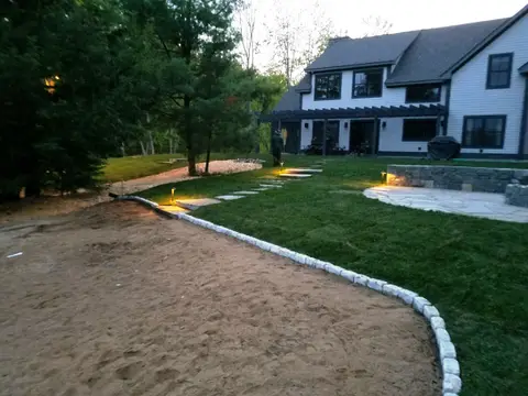 Path lights framing a paver-edged patio behind a shingled home