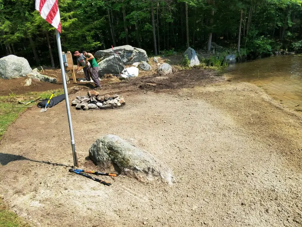 Crew building a stone fire pit at the water's edge