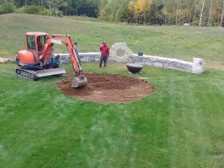 Crew excavating fire pit area beside stone wall
