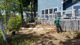 Crew member grading soil by lakeside deck