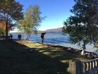 Crew raking new shoreline rock border by lake