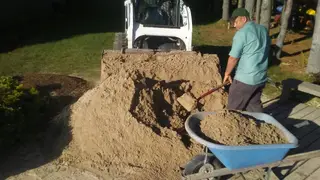 Crew shoveling sand from skid steer into wheelbarrow