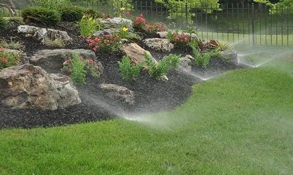 Irrigation sprinklers watering a rock garden bed